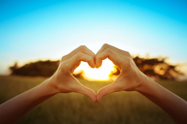 Hand shaped heart against beautiful sunset.